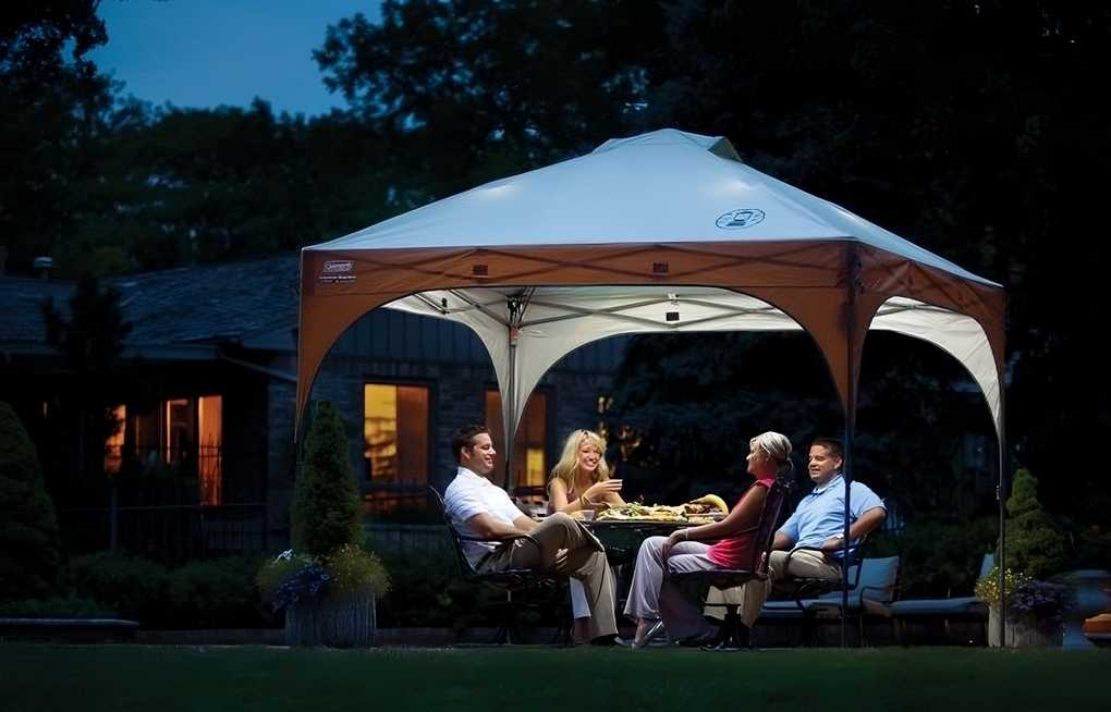 People gather around the best beach canopy, the Coleman Instant Canopy with LED Lighting System, enjoying the picnic tent with built-in LED lights.
