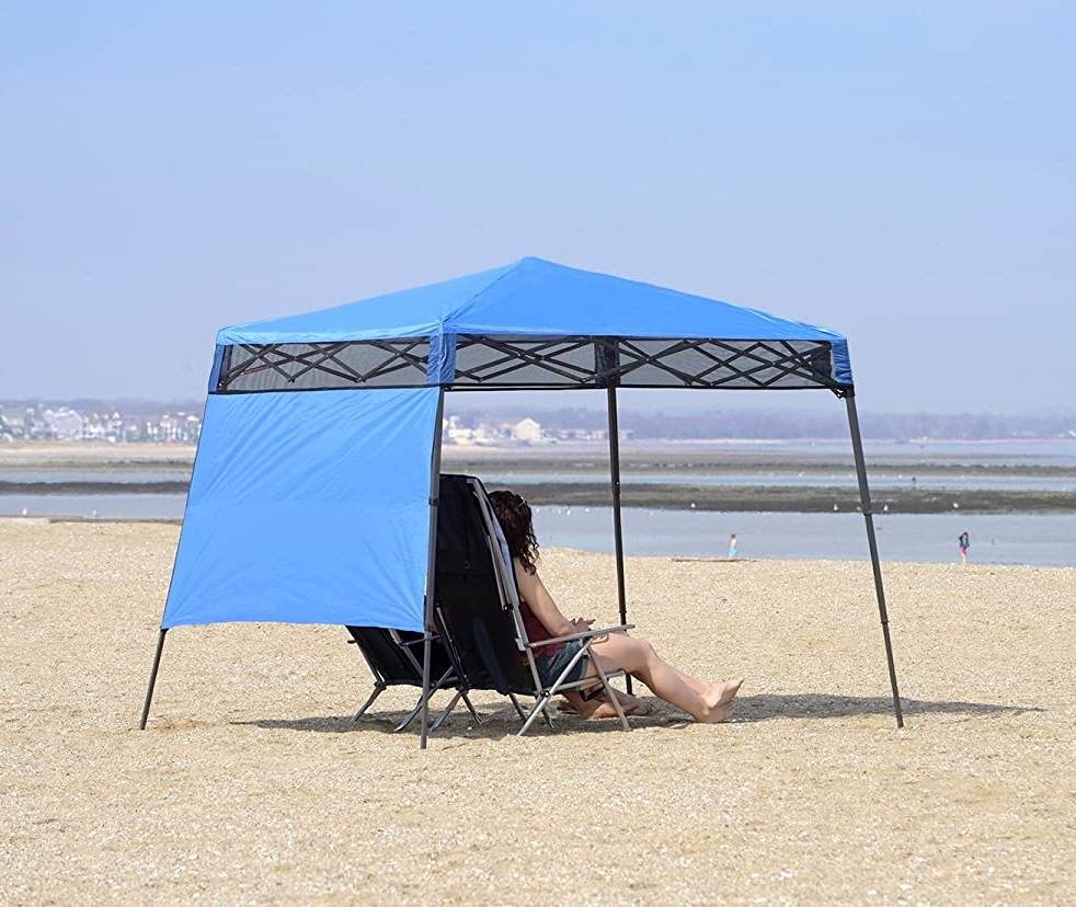 person leisurely laying on a sandy beach, comfortably sheltered beneath the Quick Shade GO Hybrid Compact Leg Bag pack Canopy. This beach shade tent provides a cool and relaxing spot, allowing the individual to enjoy the beach while protected from the sun's rays.