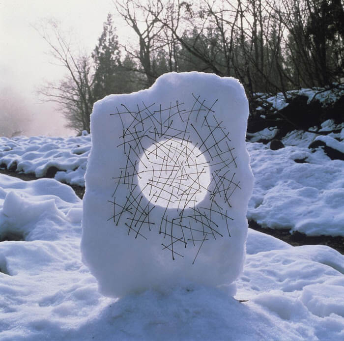 Andy Goldsworthy's ice artwork - a large snow block with a hoe in the middle and a wooden stick.