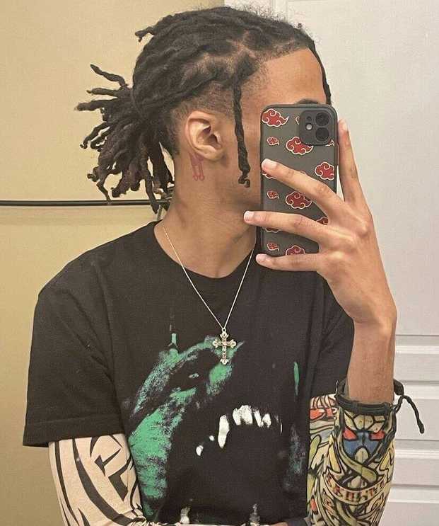 A man with braided dreads with Exposed Sides taking a picture of himself (mirror Selfie)