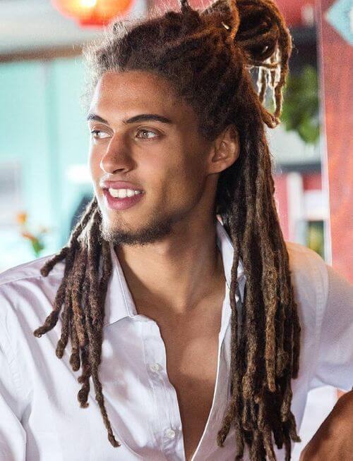 A man with half up and half down dreadlocks sitting in a restaurant.