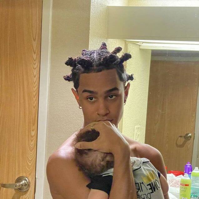 A man with Bantu knots holding a baby in his arms