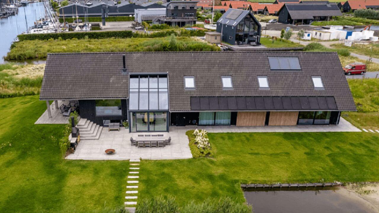 Drone view of Sustainable house Surround by Grass wide house with Windows on roof and small walkway and dinning area in Front