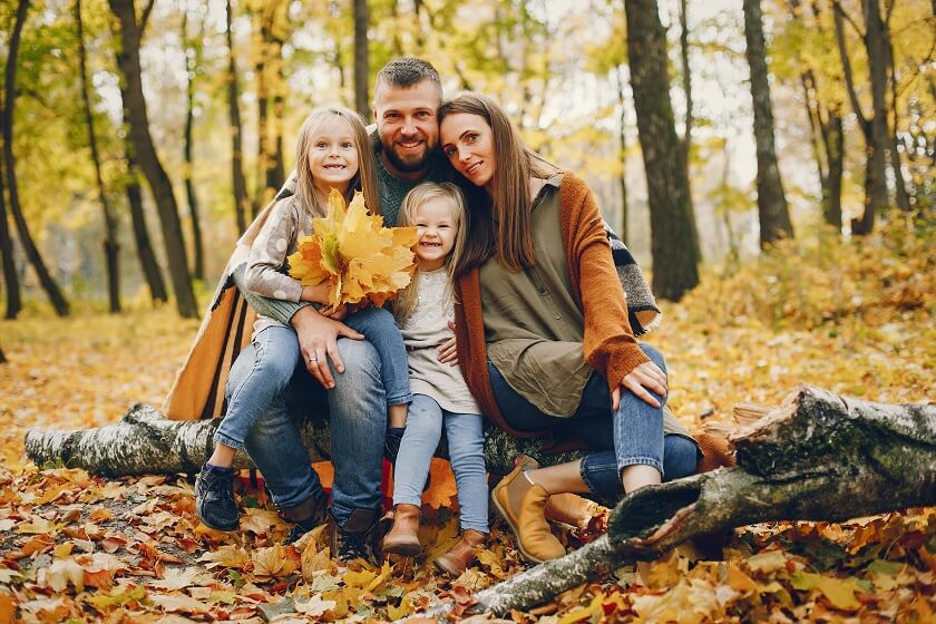 family with cute kids in autumn park sitting on Branch holding Fall leaf's