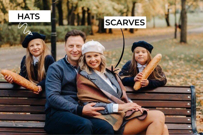 family wearing accessories like scarves or hats sitting on bench in Park with 2 child behind