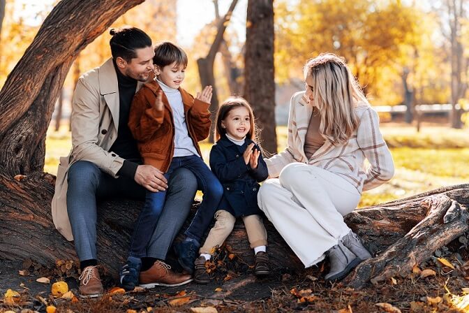 happy family autumn park mother father son daughter are sitting tree trunk wearing Autumn Outfit